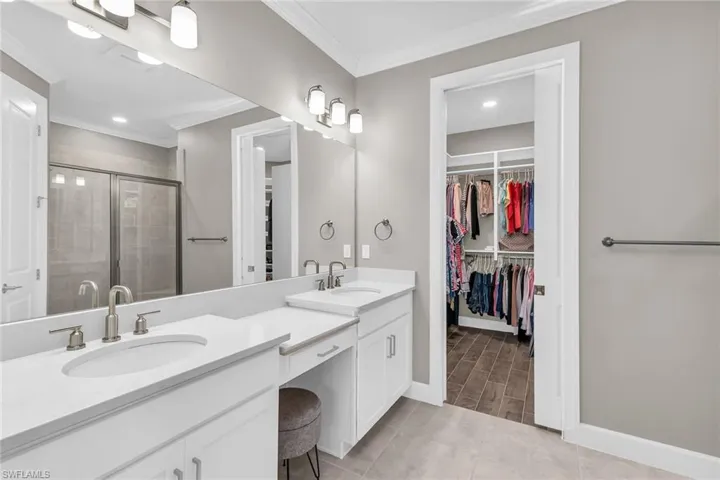 Bathroom with double vanity, a stall shower, crown molding, and a sink