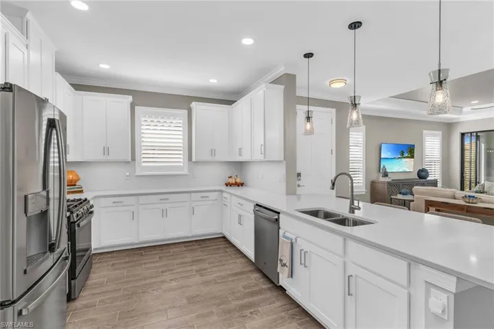 Kitchen featuring open floor plan, stainless steel appliances, light countertops, pendant lighting, and a sink