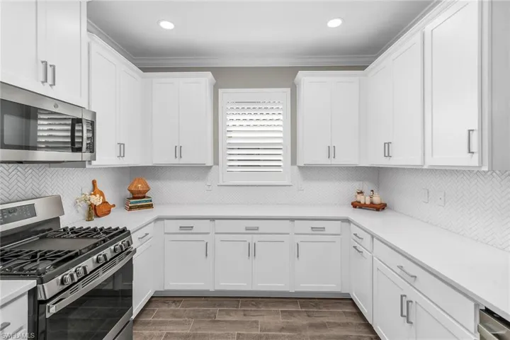 Kitchen featuring light countertops, appliances with stainless steel finishes, wood tiled floor, ornamental molding, and white cabinets