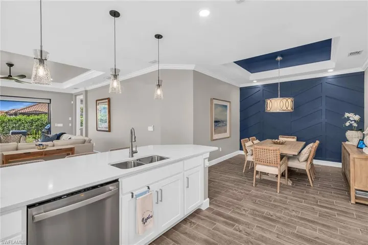 Kitchen featuring a sink, a raised ceiling, dishwasher, and hanging light fixtures
