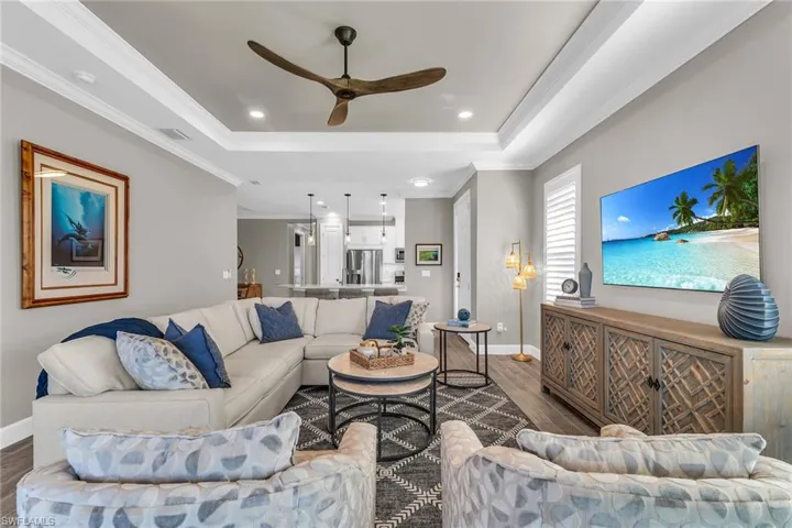 Living room with dark wood-style floors, visible vents, a raised ceiling, and crown molding