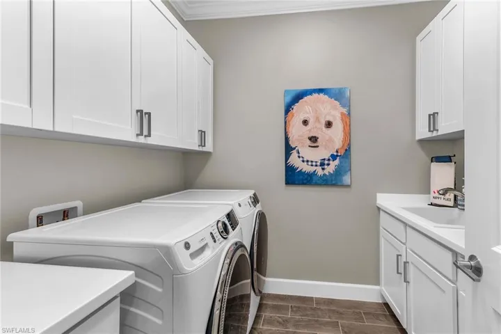 Washroom with a sink, baseboards, ornamental molding, cabinet space, and washing machine and clothes dryer