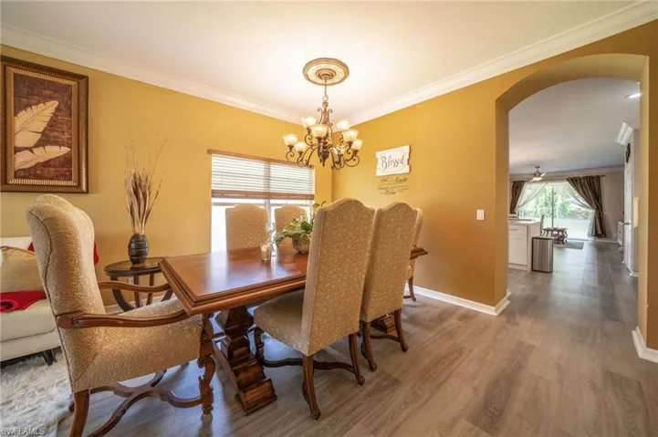 Dining space featuring arched walkways, a chandelier, wood finished floors, ornamental molding, and baseboards