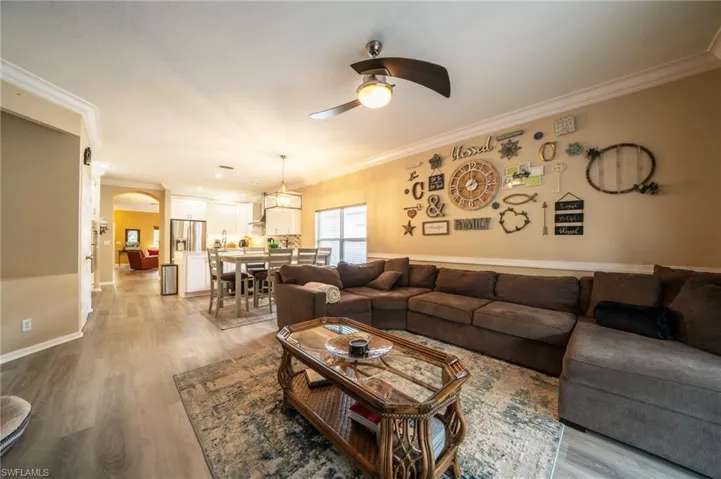Living room featuring a ceiling fan, ornamental molding, wood finished floors, arched walkways, and baseboards