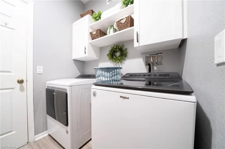 Laundry room with cabinet space, washer and dryer, a textured wall, light wood finished floors, and baseboards