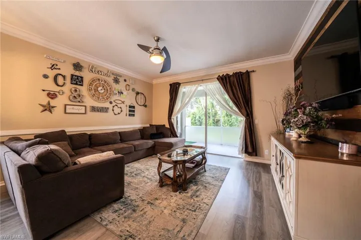 Living area with ornamental molding, a ceiling fan, dark wood-style flooring, and baseboards