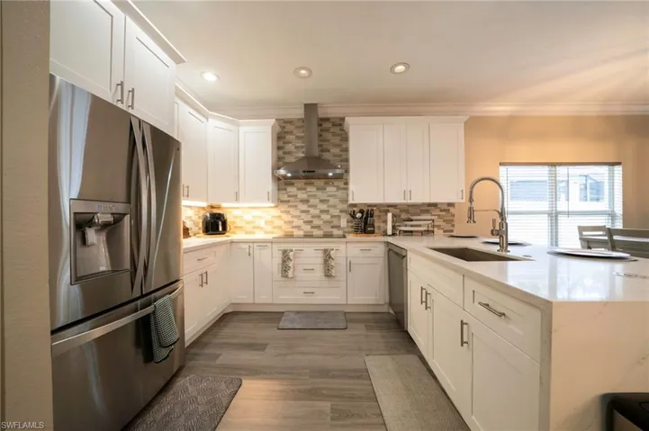 Kitchen featuring stainless steel appliances, wall chimney range hood, a sink, a peninsula, and crown molding