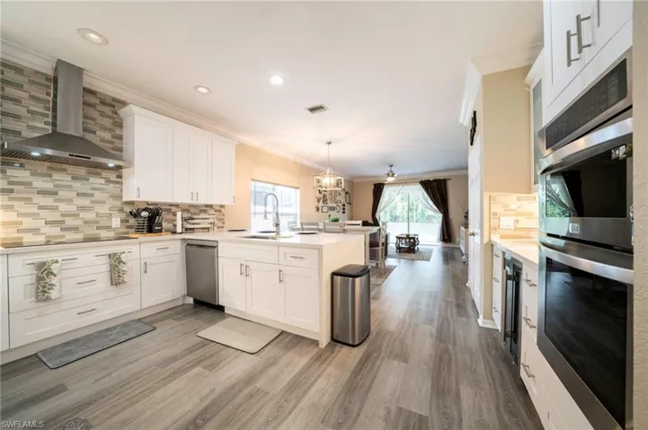 Kitchen featuring crown molding, wall chimney exhaust hood, stainless steel appliances, a peninsula, and a sink