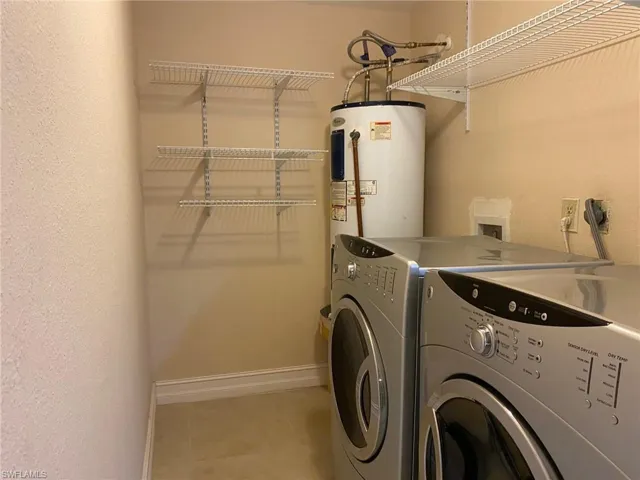 Laundry room featuring water heater, washer and clothes dryer, light tile patterned floors, and a textured wall