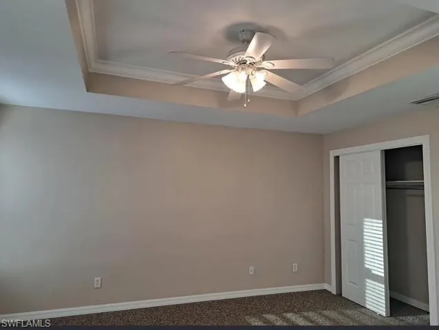 Unfurnished bedroom featuring a raised ceiling, a closet, ceiling fan, crown molding, and carpet floors