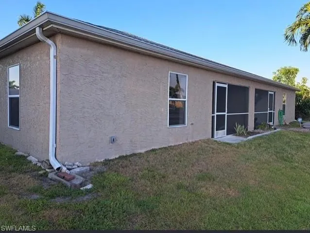 View of property exterior featuring stucco siding, a sunroom, and a lawn