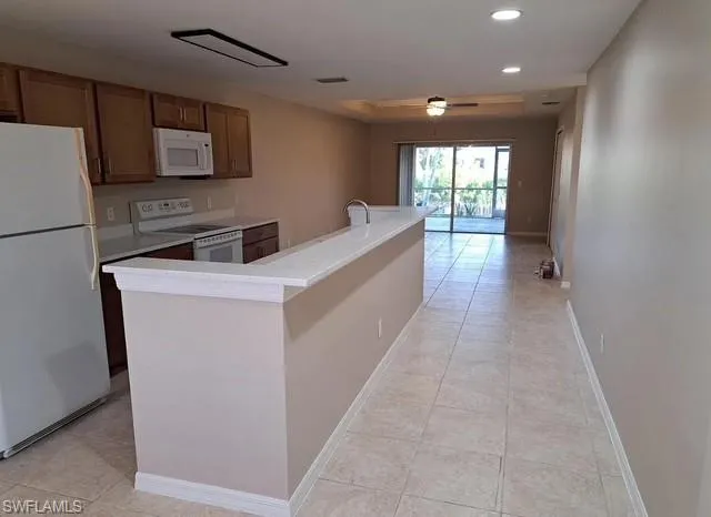 Kitchen with white appliances, light tile patterned flooring, a center island with sink, recessed lighting, and ceiling fan