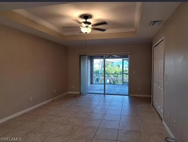Spare room with ceiling fan, light tile patterned flooring, a tray ceiling, and ornamental molding