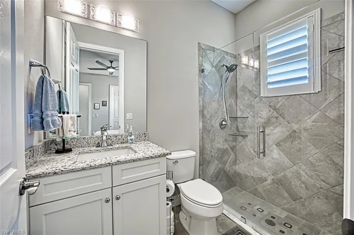 Bathroom featuring ceiling fan, toilet, vanity, tile patterned floors, and walk in shower