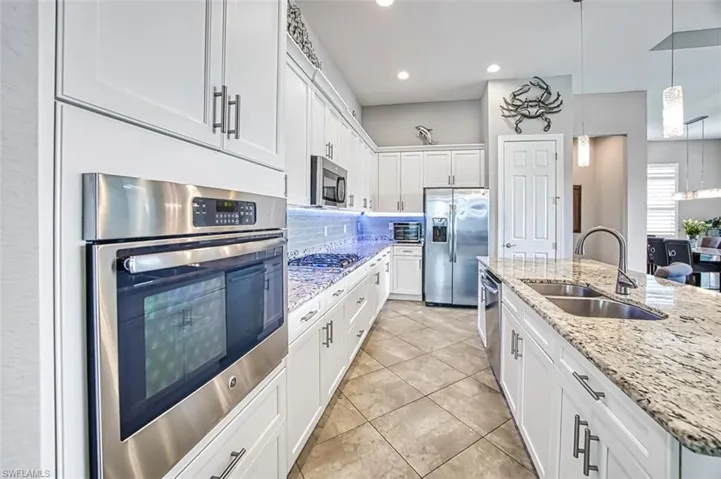 Kitchen with tasteful backsplash, white cabinets, light stone countertops, sink, and stainless steel appliances
