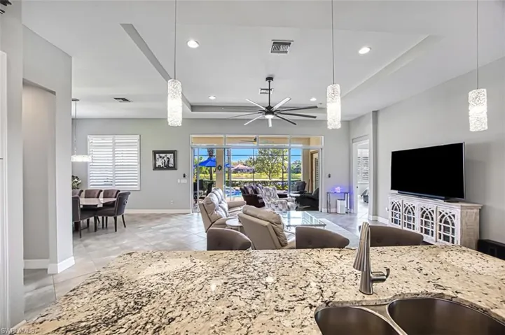 Kitchen featuring light tile patterned floors, sink, light stone counters, ceiling fan, and hanging light fixtures