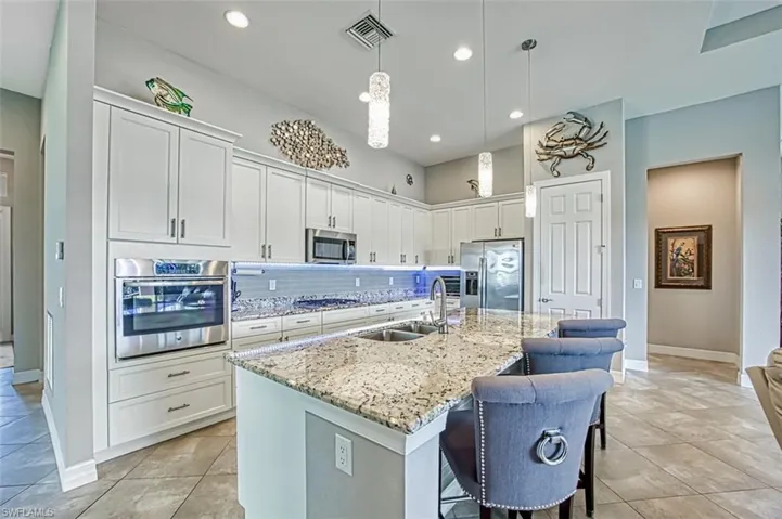 Kitchen featuring backsplash, sink, hanging light fixtures, a kitchen island with sink, and stainless steel appliances
