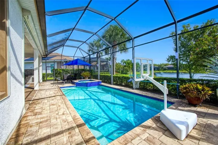 View of pool featuring glass enclosure, a patio area, and an in ground hot tub