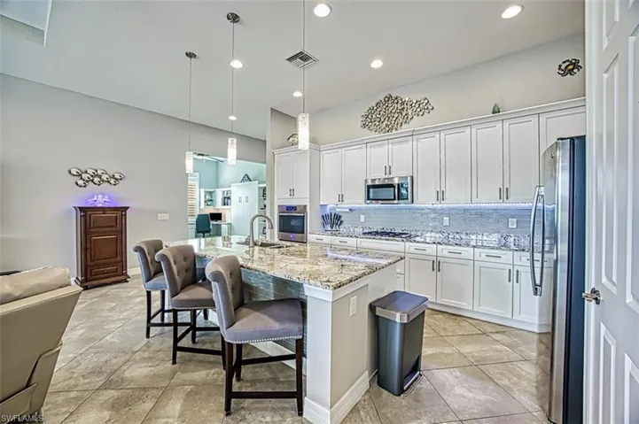Kitchen with decorative backsplash, an island with sink, white cabinetry, decorative light fixtures, and stainless steel appliances