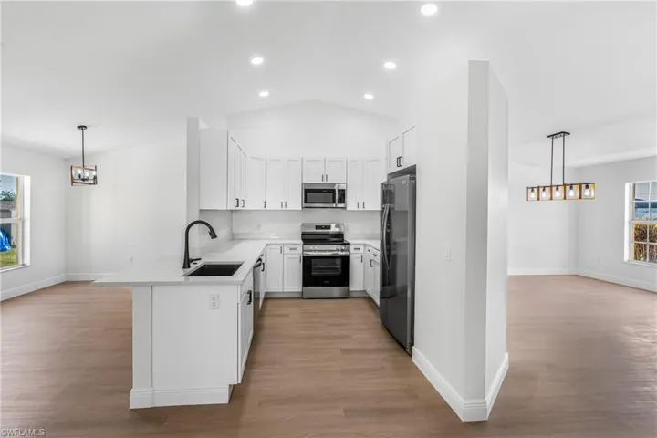 Kitchen with a chandelier, a peninsula, white cabinets, appliances with stainless steel finishes, and a sink