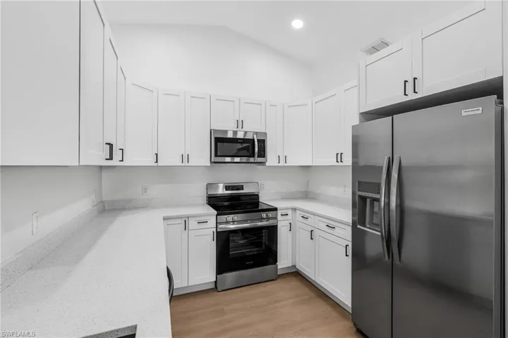 Kitchen featuring light wood-type flooring, white cabinets, visible vents, vaulted ceiling, and stainless steel appliances