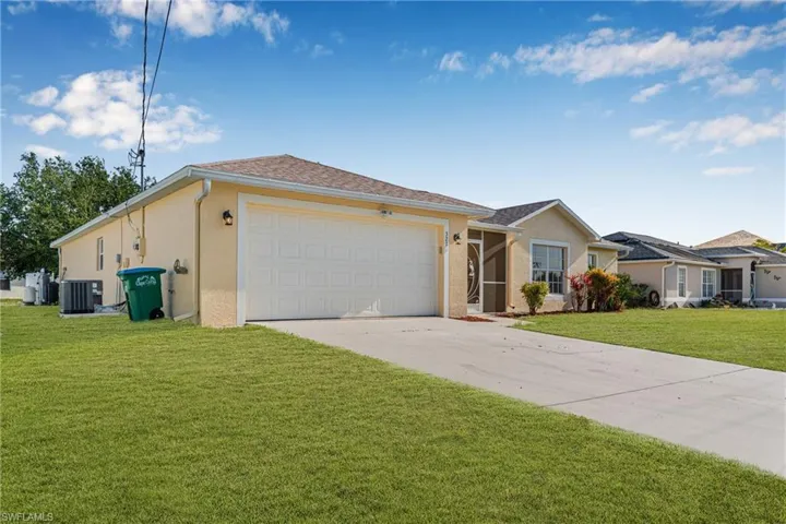 Ranch-style house with concrete driveway, central air condition unit, stucco siding, an attached garage, and a front yard