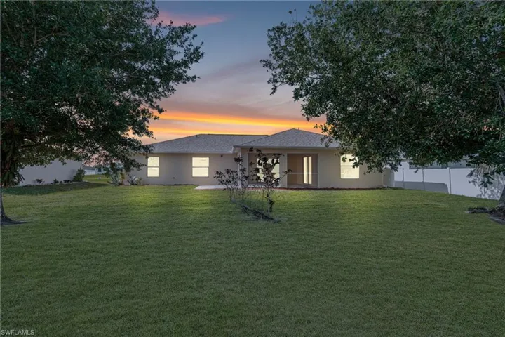 Back of property featuring roof with shingles, stucco siding, fence, and a lawn