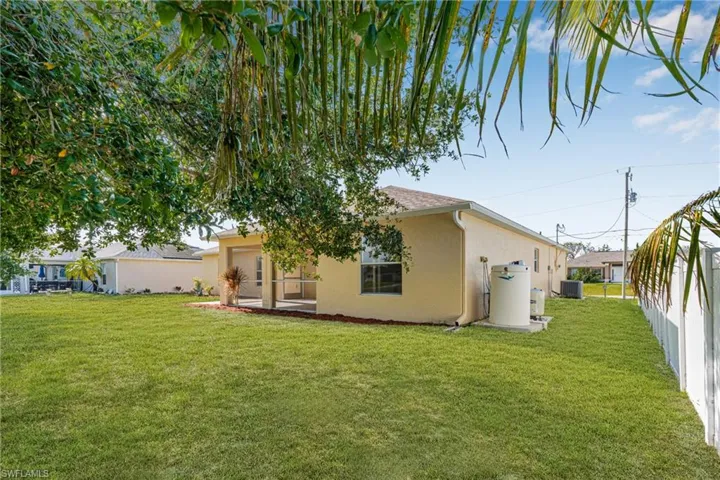 Back of property with cooling unit, stucco siding, fence, and a lawn