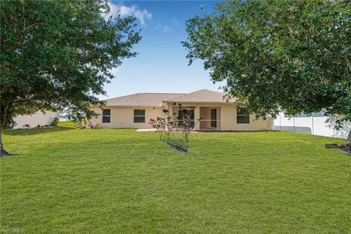 Rear view of house with a yard, stucco siding, fence, and a ceiling fan