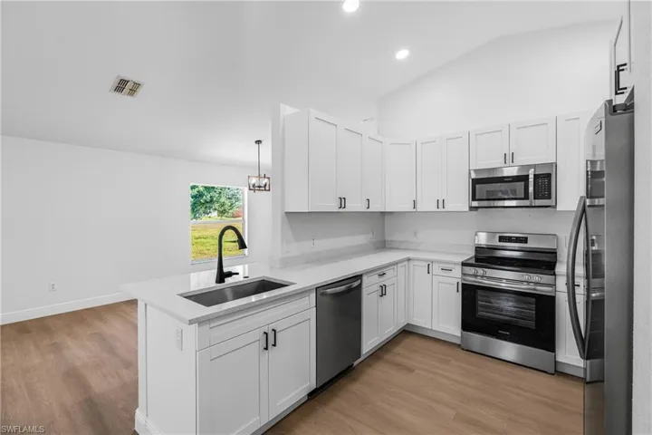 Kitchen featuring appliances with stainless steel finishes, a peninsula, visible vents, lofted ceiling, and a sink