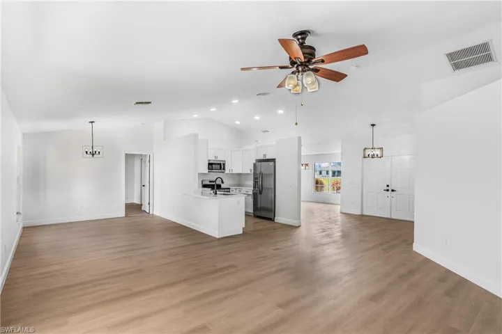 Unfurnished living room featuring light wood-type flooring, vaulted ceiling, a ceiling fan, visible vents, and a sink