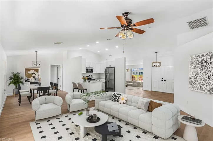 Living area with light wood finished floors, vaulted ceiling, a ceiling fan, and visible vents
