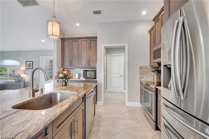 Kitchen with decorative light fixtures, light tile patterned flooring, tasteful backsplash, light stone countertops, and appliances with stainless steel finishes