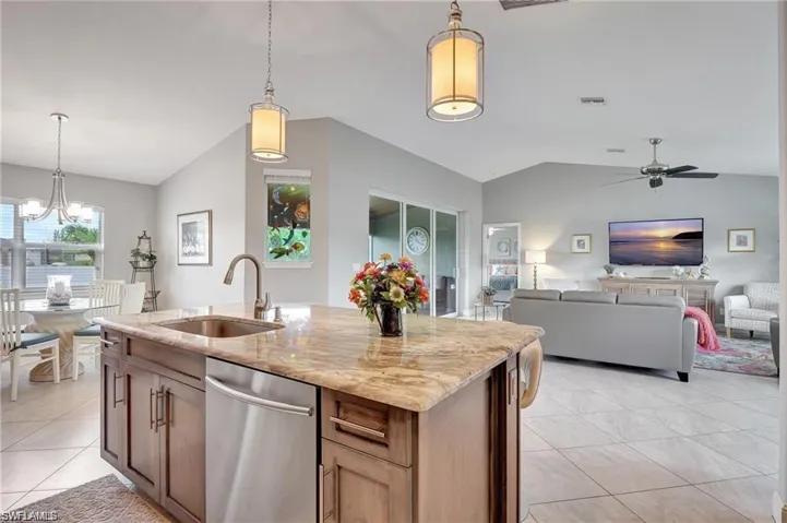 Kitchen featuring stainless steel dishwasher, pendant lighting, sink, vaulted ceiling, and a kitchen island with sink