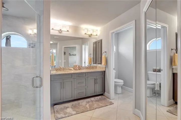 Bathroom featuring dual vanity, toilet, a shower with door, and tile patterned flooring