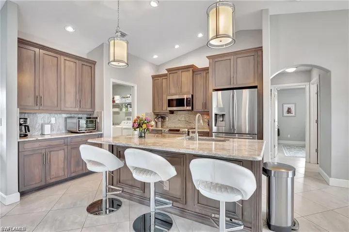 Kitchen featuring vaulted ceiling, an island with sink, appliances with stainless steel finishes, decorative backsplash, and decorative light fixtures