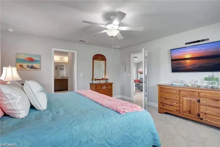 Bedroom with light tile patterned flooring, connected bathroom, and ceiling fan