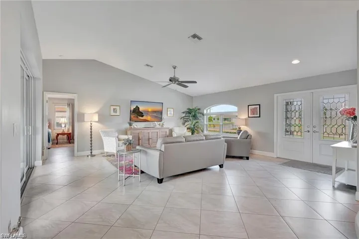 Tiled living room with french doors, ceiling fan, and vaulted ceiling