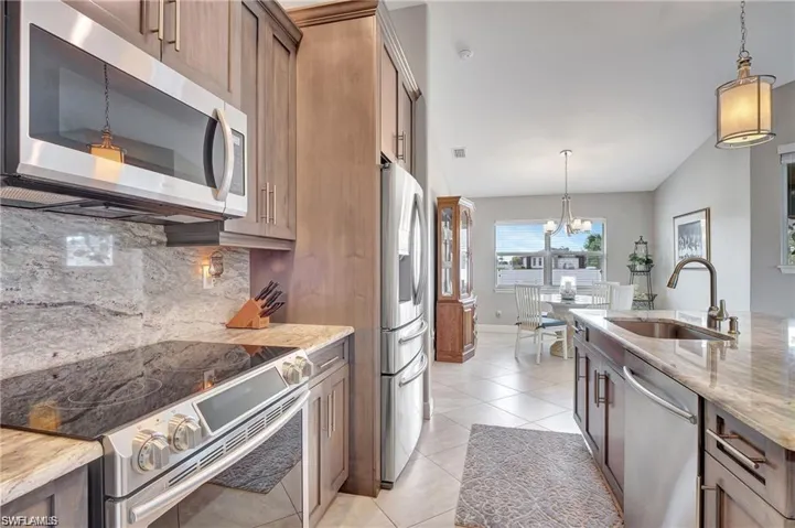 Kitchen featuring appliances with stainless steel finishes, sink, pendant lighting, light stone counters, and backsplash