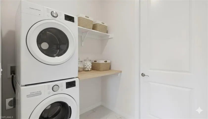 Laundry area featuring stacked washing machine and dryer and light marble finish flooring
