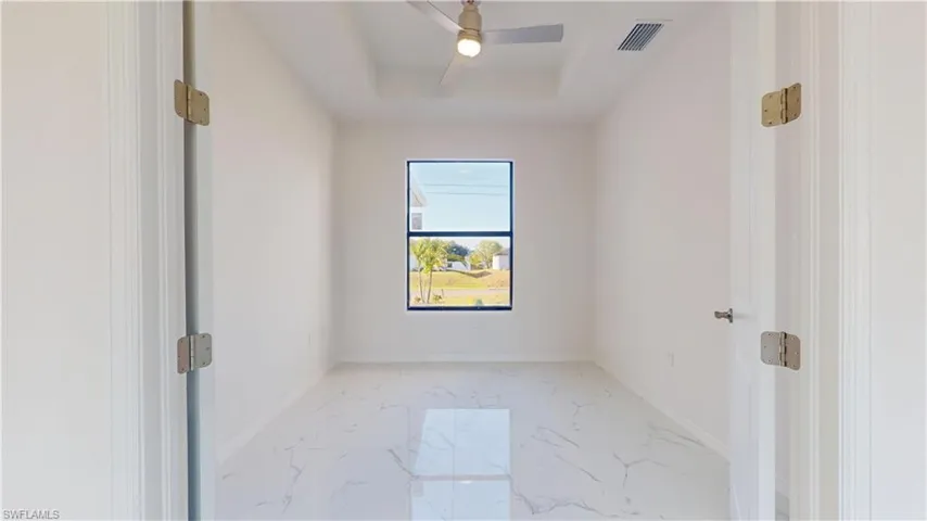 Unfurnished room featuring light marble finish flooring, a raised ceiling, and ceiling fan