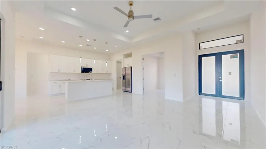 Unfurnished living room featuring french doors, light marble finish flooring, recessed lighting, a tray ceiling, and a ceiling fan