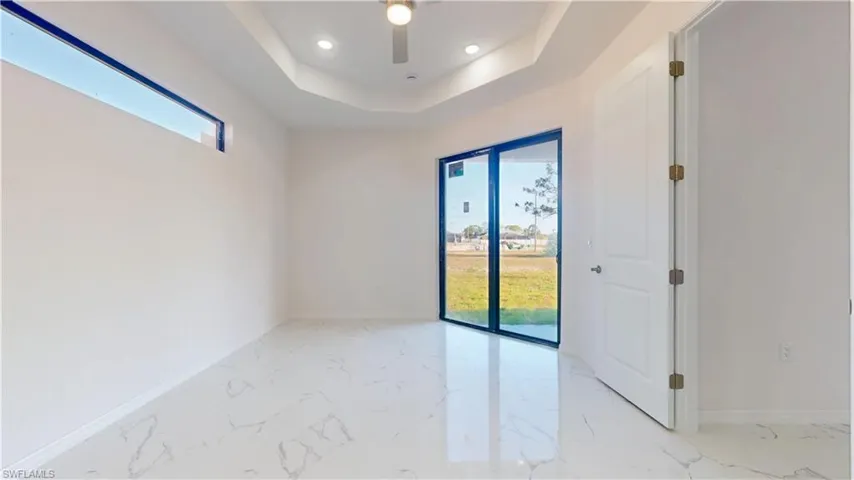 Empty room with light marble finish flooring, a tray ceiling, recessed lighting, and ceiling fan