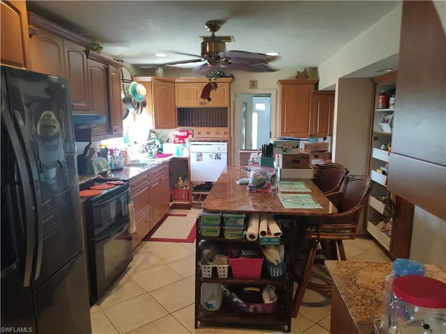 Kitchen with ceiling fan, light tile patterned floors, stone countertops, and black appliances