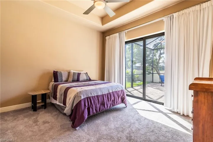 Carpeted bedroom featuring a raised ceiling, ceiling fan, and access to exterior