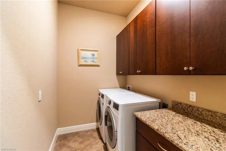 Clothes washing area with cabinets, washer and dryer, and light tile patterned flooring