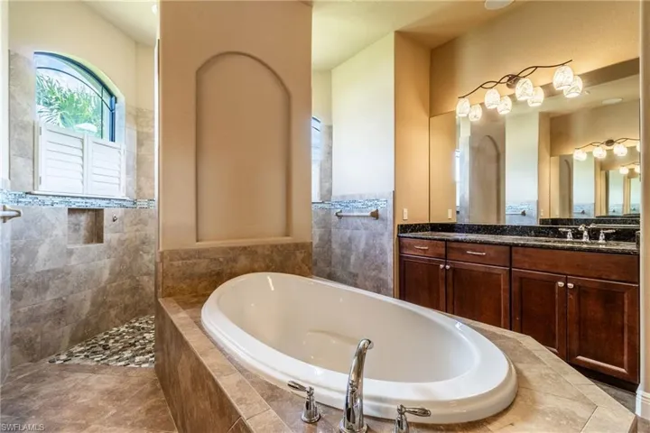 Bathroom with tile walls, tile patterned floors, vanity, and a relaxing tiled tub