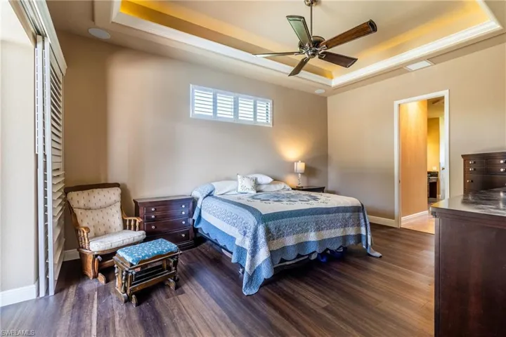 Bedroom with dark wood-type flooring, ceiling fan, and a raised ceiling