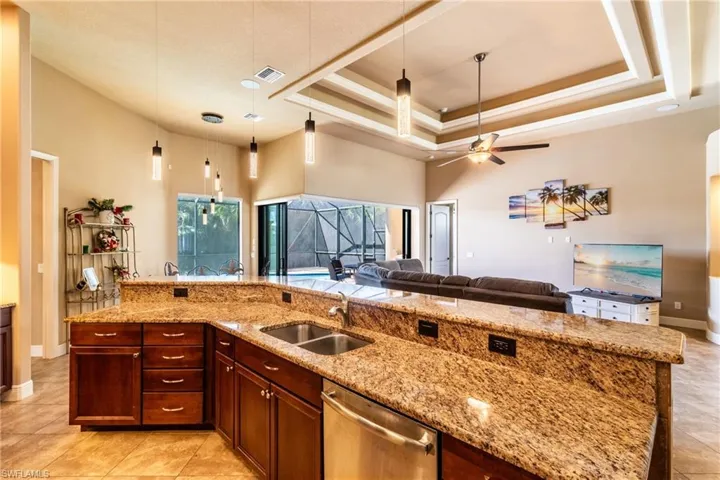 Kitchen featuring stainless steel dishwasher, sink, light stone counters, and a spacious island