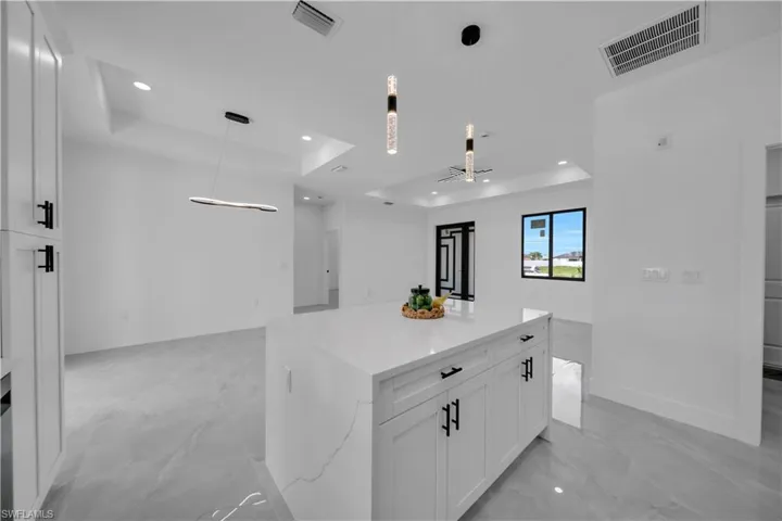 Kitchen featuring a raised ceiling, open floor plan, recessed lighting, white cabinetry, and light marble finish floors